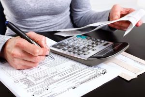 Foto de uma mão escrevendo em um papel e calculando notas, representando o momento de contratar uma contabilidade