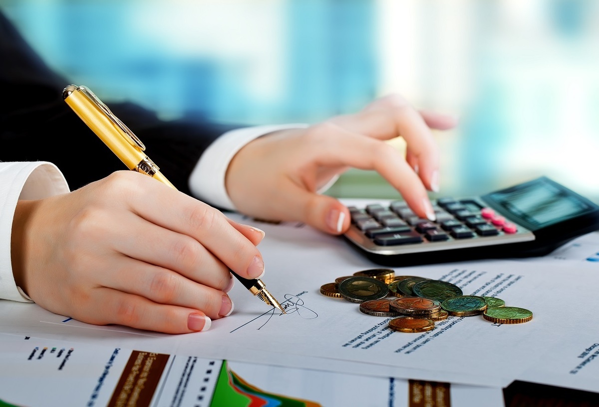 Foto de uma mão feminina anotando em um papel as contas que faz em uma calculadora, representando o financiamento com consultoria jurídica