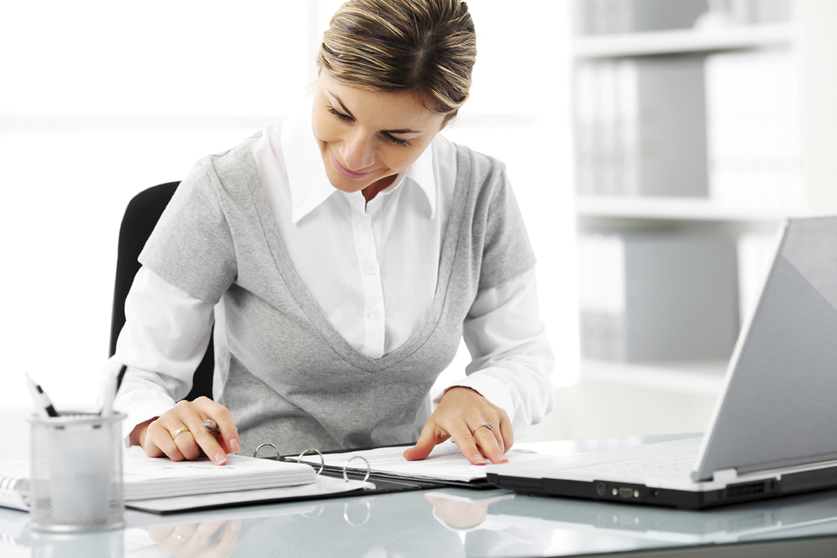 Foto de uma mulher formal checando um caderno com um notebook ao lado, representando como obter um cnpj