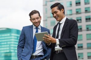 Dois homens vestidos com terno mexendo em um tablet, representando o pagamento do boleto do MEI online