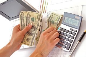 Foto de uma pessoa contando dinheiro com uma calculadora ao lado, representando a diferença entre faturamento e lucro