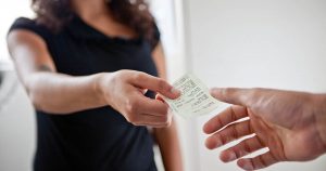 Foto de uma mulher entregando uma nota fiscal para outra pessoa, representando o processo para cancelar Nota Fiscal de Serviço Eletrônica