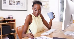 Foto de uma mulher trabalhando de casa, bebendo café e fazendo anotações, representando o número de empresas criadas