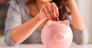 Foto de uma mulher colocando uma moeda em um cofre de porquinho, representando as finanças em dia