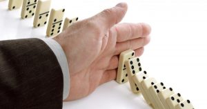Foto de uma mão masculina parando uma sequência de peças de dominó, representando a gestão de crise