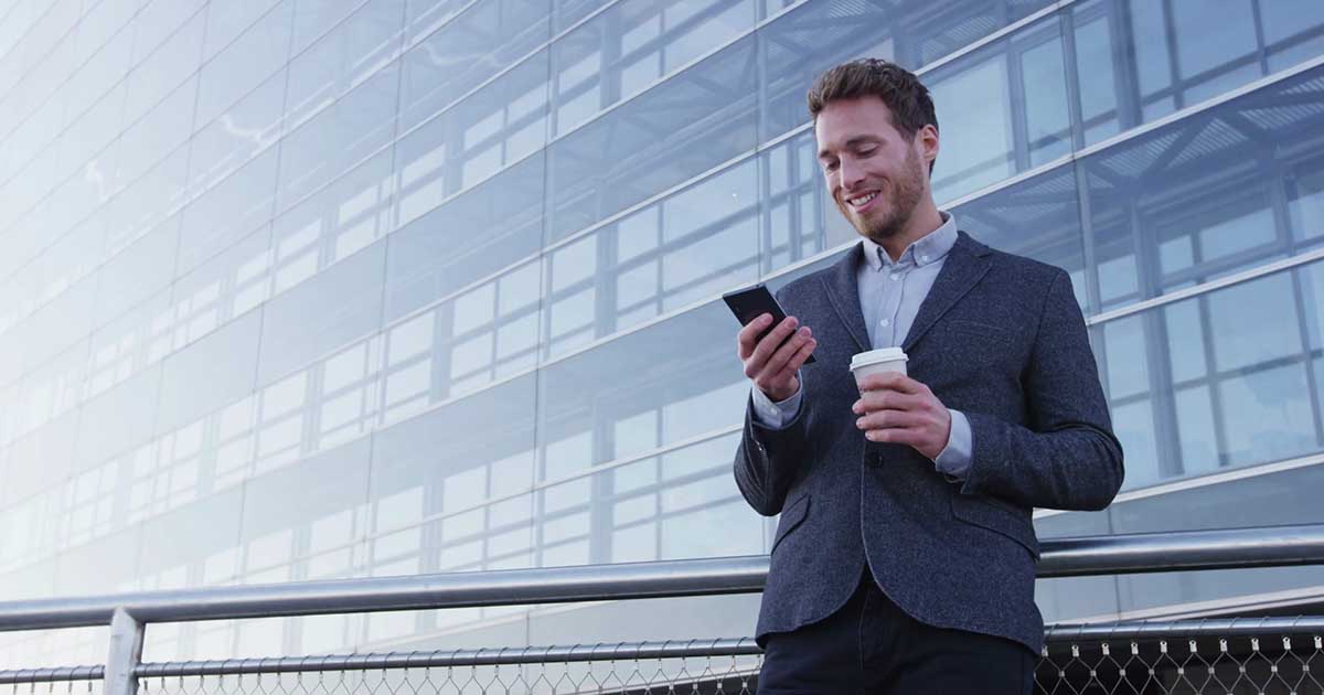 Foto de um homem em pé tomando café e mexendo no celular representando o mobile marketing