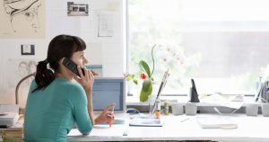 Foto de uma mulher trabalhando de casa e falando ao telefone, representando as novas regras para MEI