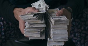 Foto de um homem segurando dois amontoados de dinheiro, representando os hábitos dos milionários