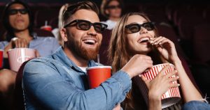 Foto de um casal comendo pipoca e sorrindo, representando como abrir um cinema