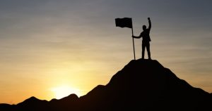 foto de um homem em cima de uma montanha com uma bandeira, representando os empreendedores de sucesso