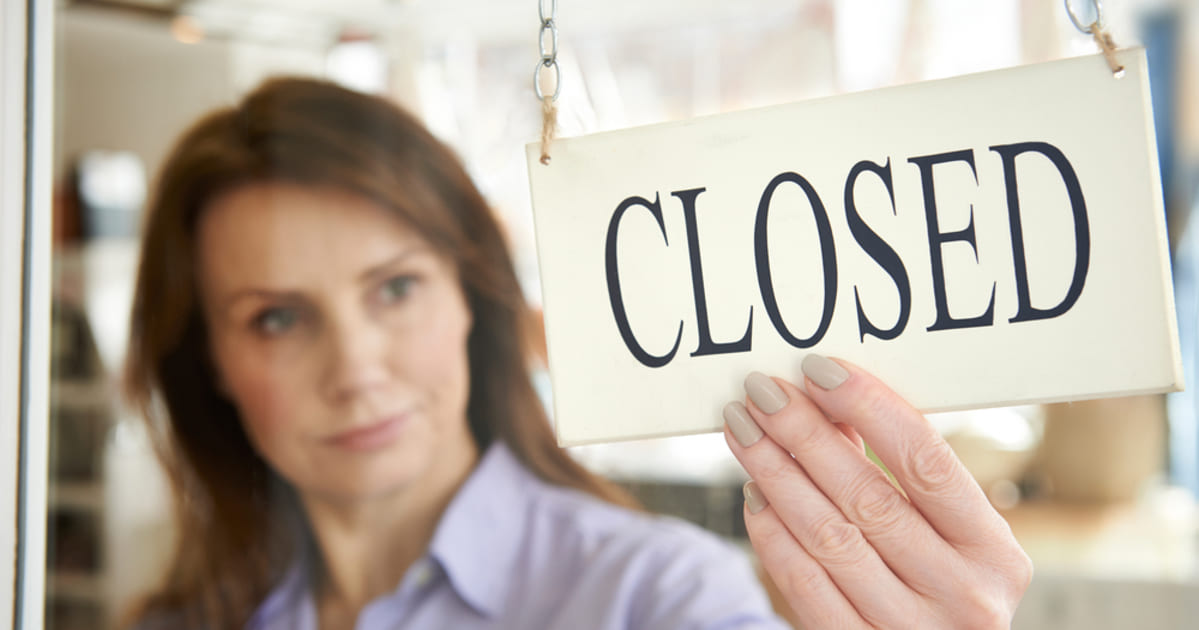 Foto de uma mulher segurando uma placa de loja escrita "fechado", representando as empresas fechadas