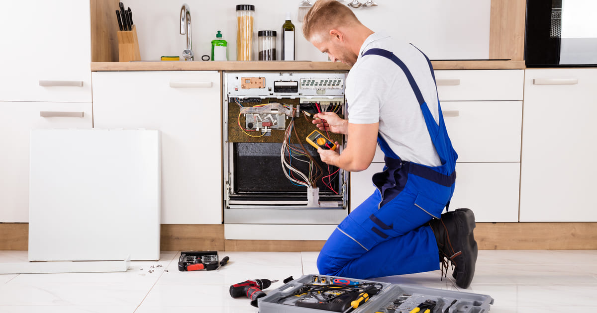 Foto de um homem arrumando um fogão depois que ele iniciou seu projeto de como montar um serviço de manutenção de eletrodomésticos
