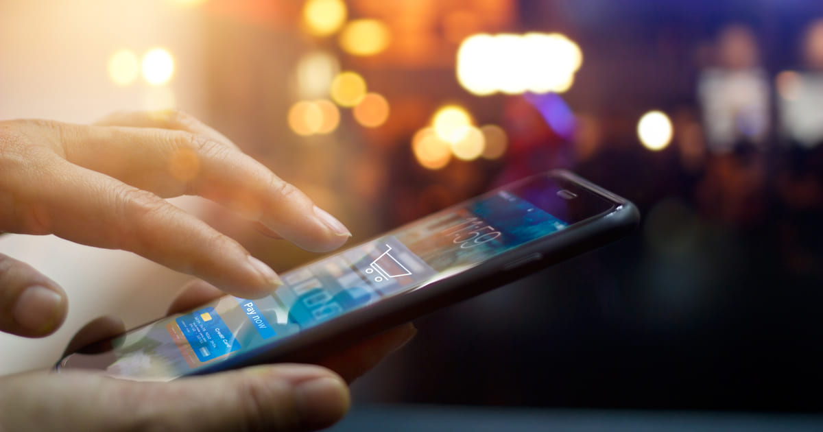 Imagem de um homem com um celular na mão comprando algo por um aplicativo para remeter ao m-commerce retratado no texto