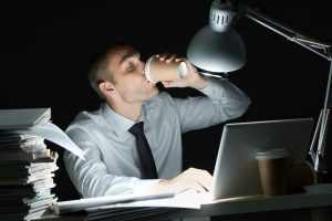 foto de um homem trabalhando a noite com um copo de café, representando como calcular hora extra